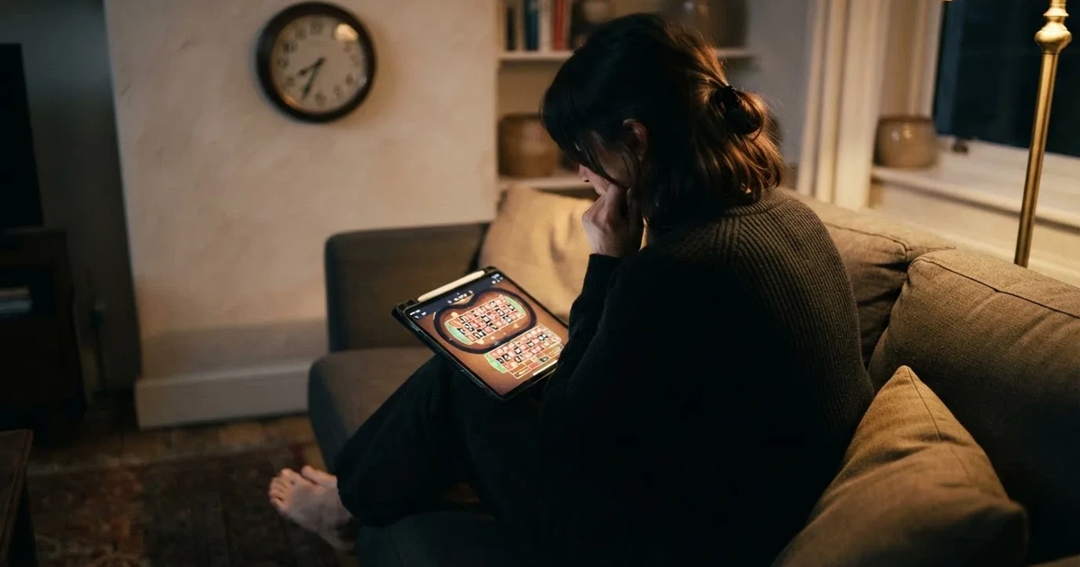 Pessoa num sofá a olhar pensativa para um tablet, com um relógio na parede atrás — ofertas de casino em portugal